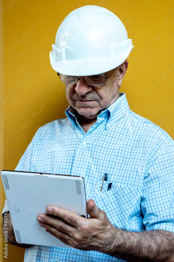 Man in a white shirt and engineer helmet holding a tablet with a yellow background. Man in a white shirt and engineer helmet holding a tablet with a yellow background.