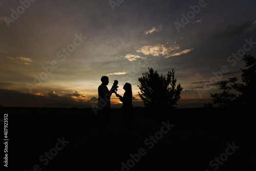 Young parents hug and kiss their newborn daughter in nature. Silhouette of parents and newborn baby at sunset.