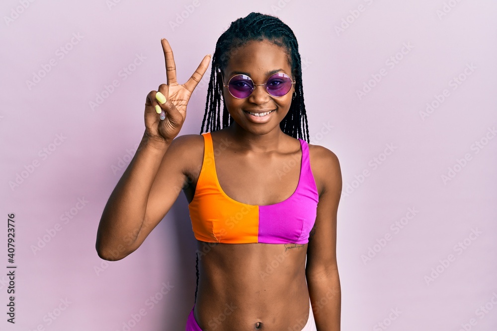 Young african american woman wearing bikini and sunglasses showing and pointing up with fingers number two while smiling confident and happy.