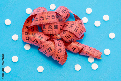 Measuring centimeter tape is on blue background surrounded by white round tablets. Concept photo pharmacological weight loss and use of medicines such as sibutramine, orlistat, metformin photo