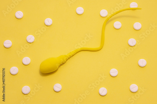 The yellow sperm model is on a yellow polka-dotted background made with white pills. Concept of diagnosis and treatment of male infertility and sperm problems photo