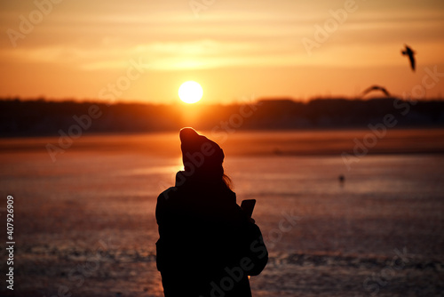 Silhouette of girl on sunset background making photo winter