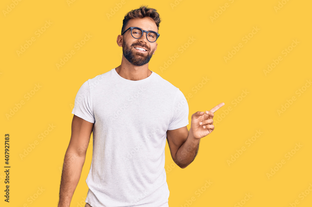 Young hispanic man wearing casual clothes and glasses with a big smile on face, pointing with hand finger to the side looking at the camera. Young hispanic man wearing casual clothes and glasses with a big smile on face, pointing with hand finger to the side looking at the camera.