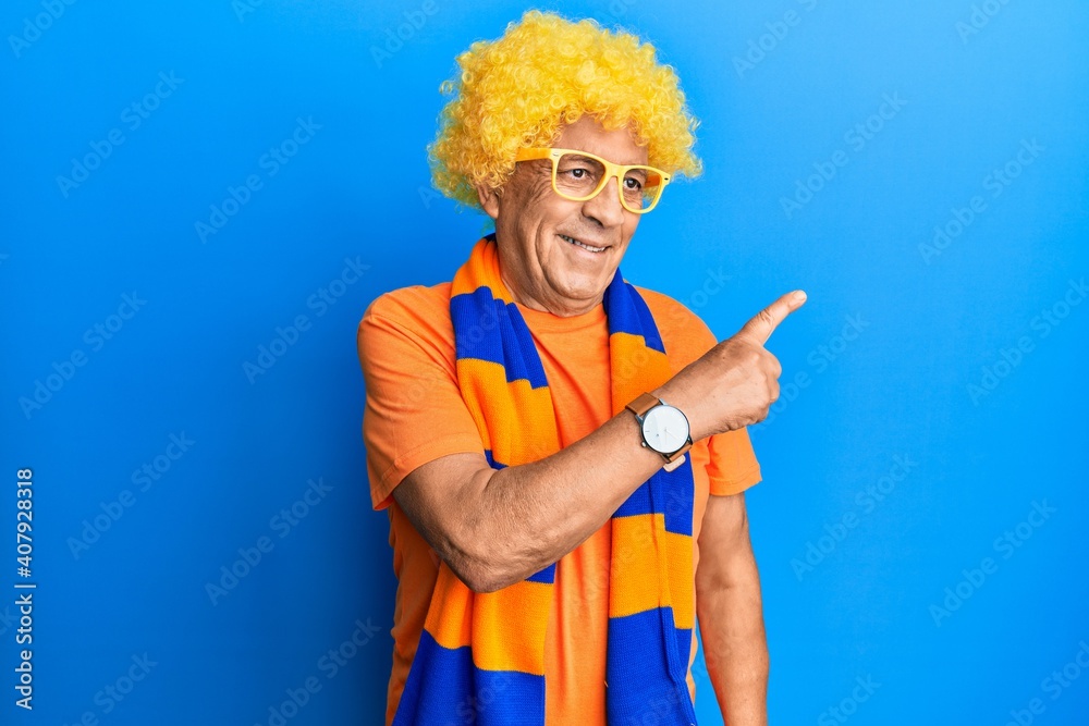 Senior hispanic man football hooligan cheering game smiling cheerful pointing with hand and finger up to the side