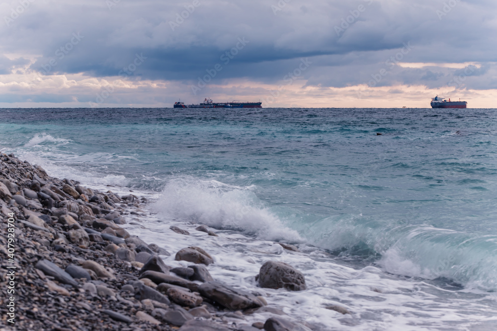 The tanker ship sails on the sea horizon. Stone coast and sea waves in the foreground