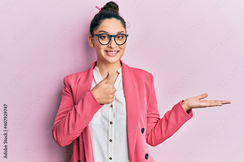 Beautiful middle eastern woman wearing business jacket and glasses showing palm hand and doing ok gesture with thumbs up, smiling happy and cheerful