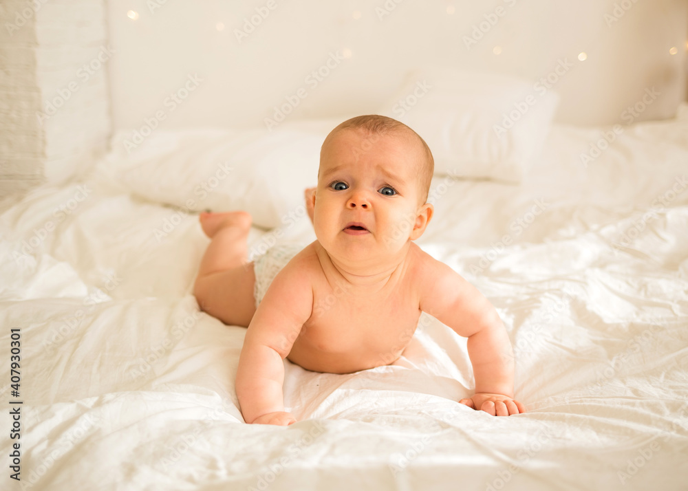 upset little baby girl in a diaper lying on her stomach on the bed upset little baby girl in a diaper lying on her stomach on the bed