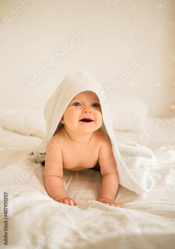 smiling little baby girl in a white bath towel lying on the bed
