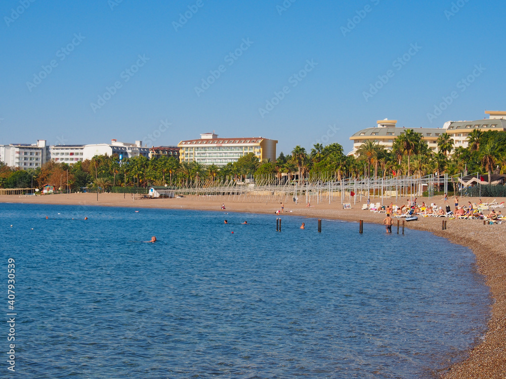 Alanya, Turkey - 11.14.2020. People on the beach, blue sea, green trees and palms . Copy space for text.