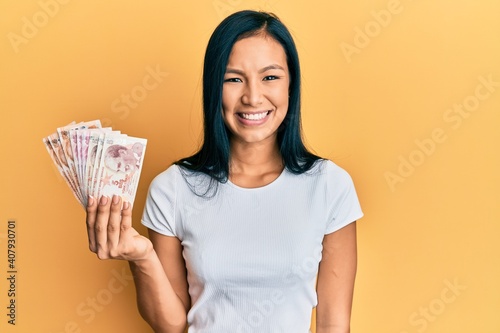 Beautiful hispanic woman holding 5 turkish lira banknotes looking positive and happy standing and smiling with a confident smile showing teeth