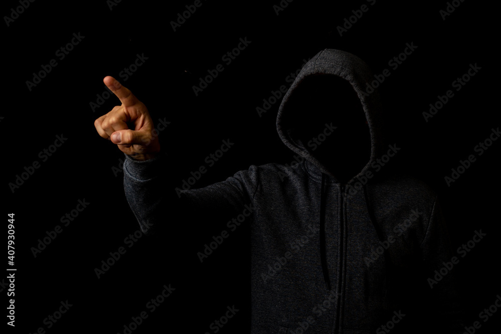 Man without a face in a hood touches his finger on a dark background