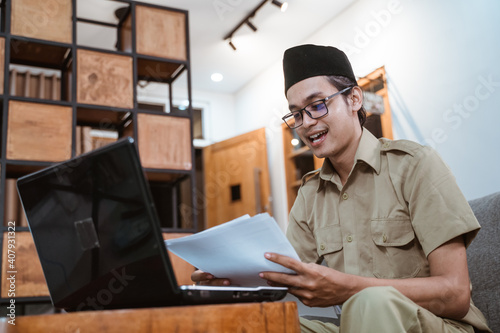 man in government uniform holding papers while working from home online using laptop computer