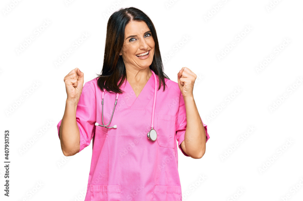 Middle age brunette woman wearing doctor uniform and stethoscope screaming proud, celebrating victory and success very excited with raised arms Middle age brunette woman wearing doctor uniform and stethoscope screaming proud, celebrating victory and success very excited with raised arms
