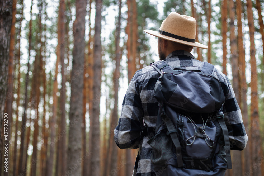 Young Man in a hat with a backpack in a pine forest. Hike in the mountains or forest