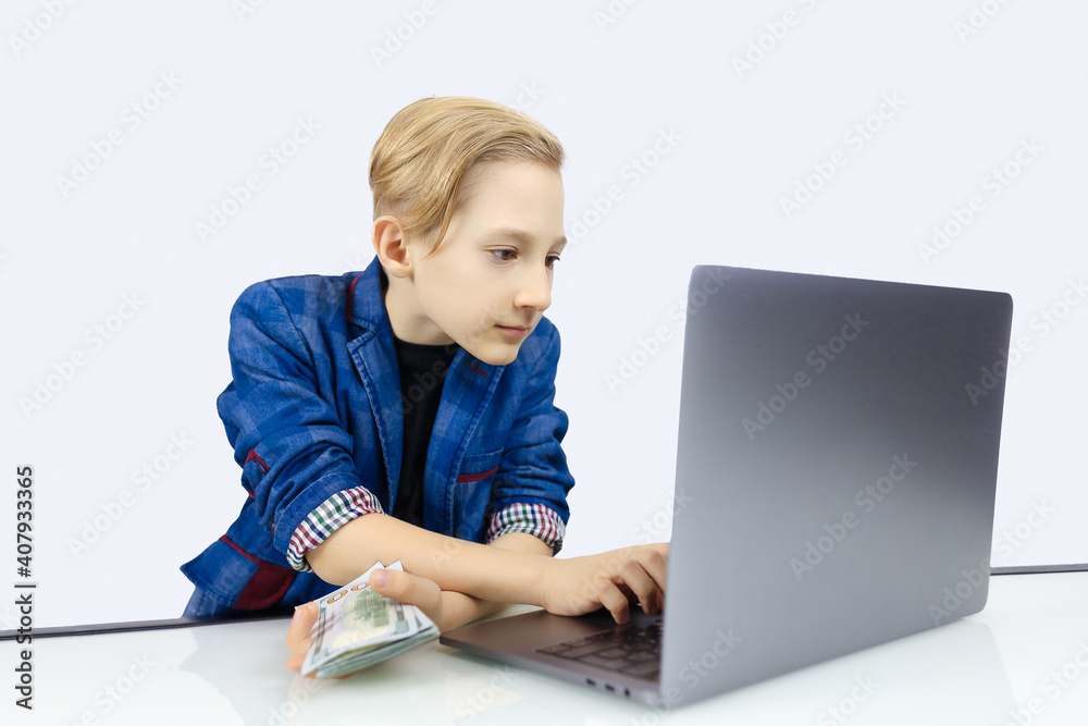 a boy in a jacket works at a laptop and holds banknotes in his hand a boy in a jacket works at a laptop and holds banknotes in his hand