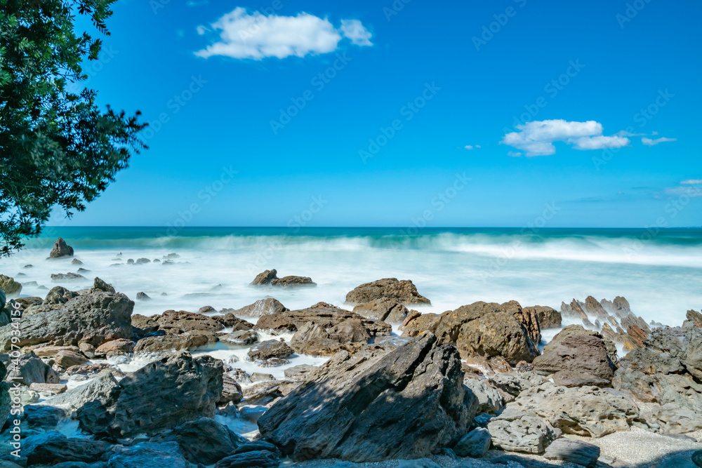 Whitewater from surf smoothed as it breaks around rugged coast at base of Mount Maunganui, New zealand