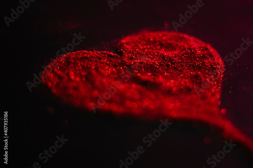 Blurred red heart made of sparkles on a black background.