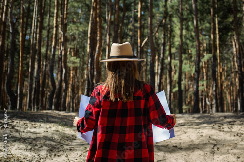 Woman with hat and red plaid shirt holding a map in the forest © Alex