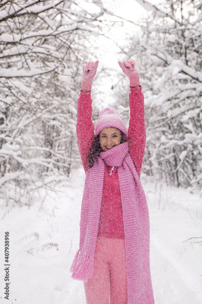Obraz premium woman in pink clothes a jacket a knitted scarf and a hat stands in a snowy forest in winter