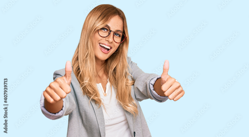 Beautiful blonde young woman wearing business clothes approving doing positive gesture with hand, thumbs up smiling and happy for success. winner gesture.