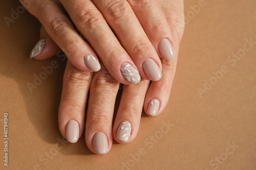 Hands of an adult woman with a new manicure. Hands with beige nail polish on a brown background. Shallow depth of field