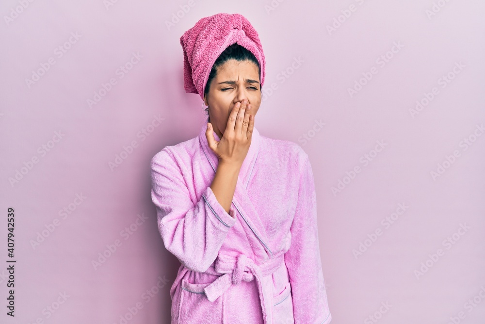 Young hispanic woman wearing shower towel cap and bathrobe bored yawning tired covering mouth with hand. restless and sleepiness.
