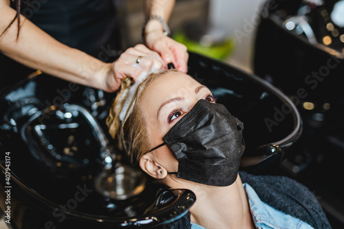 Beautiful middle-aged woman with protective face mask in hair salon.