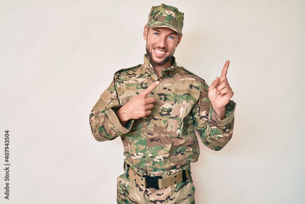 Young caucasian man wearing camouflage army uniform smiling and looking at the camera pointing with two hands and fingers to the side.