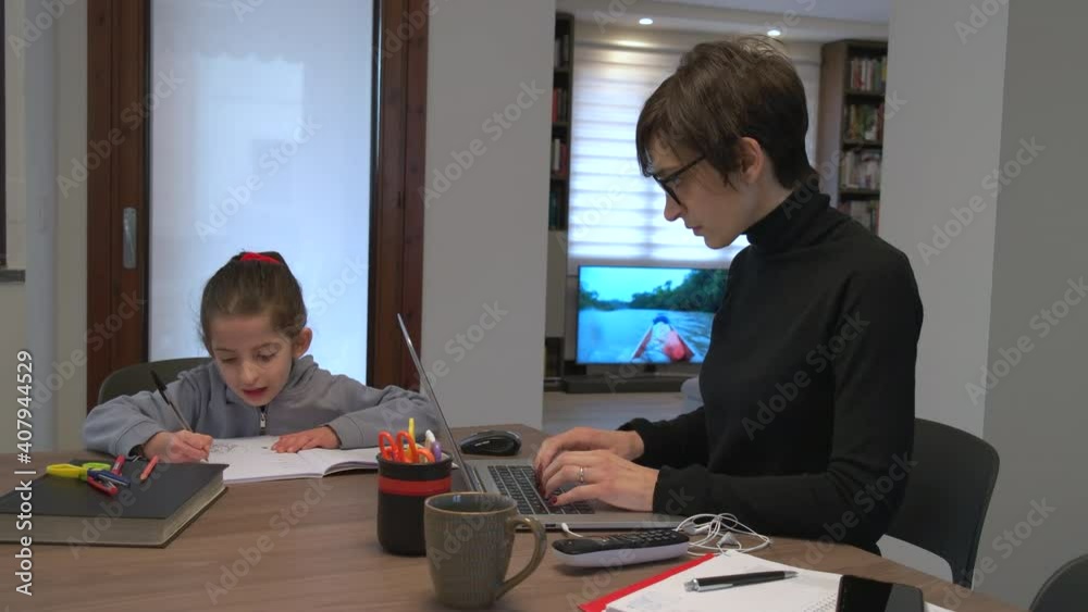 Business woman working from home with laptop computer and helping little girl with school homework. Multitasking mother doing remote work with pc and daughter studying during Covid-19 lockdown