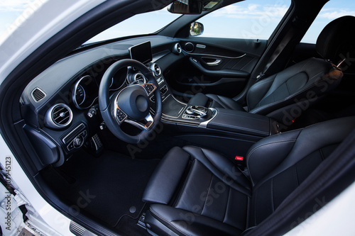 The car is inside. The interior of a prestigious modern car. Front seats with steering wheel, dashboard and display. black leather interior with black dashboard. on sky background