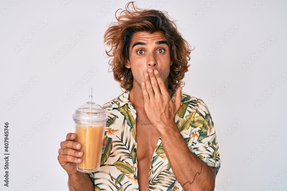 Young hispanic man wearing summer shirt drinking glass of orange juice covering mouth with hand, shocked and afraid for mistake. surprised expression Young hispanic man wearing summer shirt drinking glass of orange juice covering mouth with hand, shocked and afraid for mistake. surprised expression