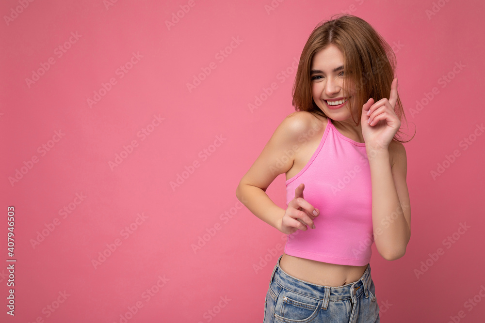 Young happy beautiful dark blonde woman with sincere emotions isolated on background wall with copy space wearing stylish pink top and dancing. Positive concept Young happy beautiful dark blonde woman with sincere emotions isolated on background wall with copy space wearing stylish pink top and dancing. Positive concept