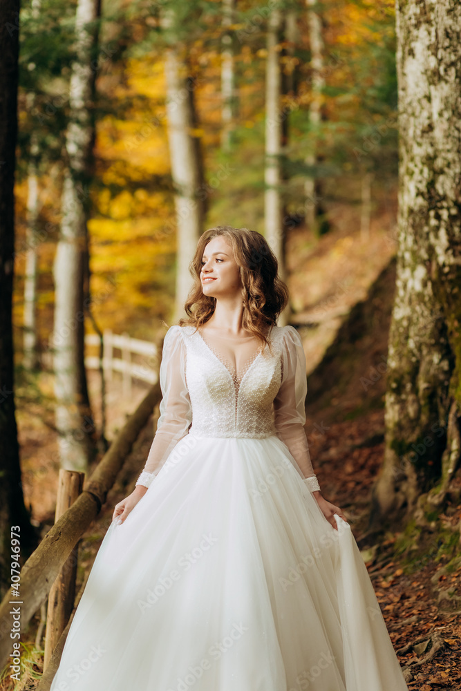Beautiful bride with wavy hair walks on a trail in autumn park.