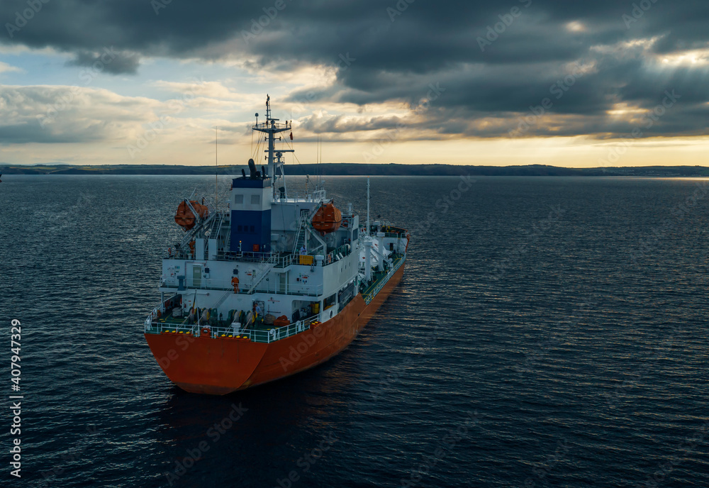 Gas carrier at sea sailing close to coastline and beautiful sunset.