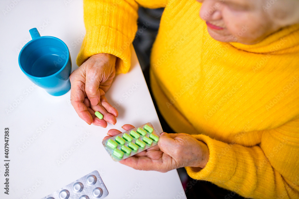 Obraz premium Ill old woman taking a pill from a pill dispenser in her house