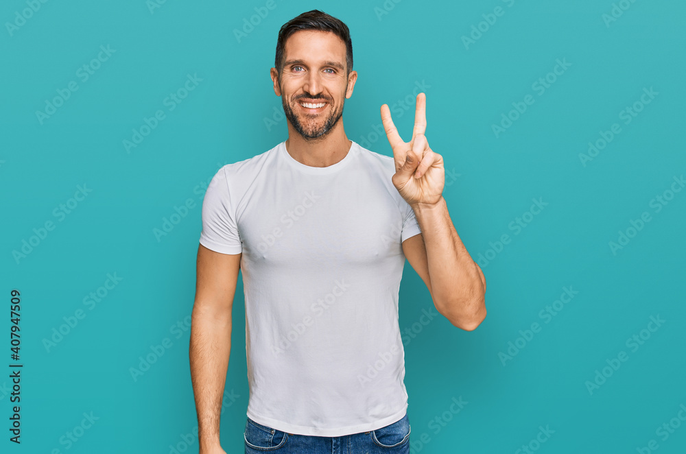 Handsome man with beard wearing casual white t shirt showing and pointing up with fingers number two while smiling confident and happy. Handsome man with beard wearing casual white t shirt showing and pointing up with fingers number two while smiling confident and happy.