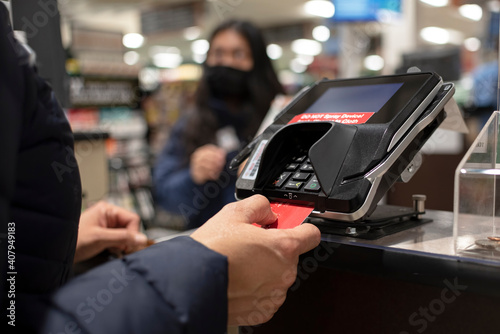 Close-up of a female hand inserting credit card in a smartphone at supermarket.