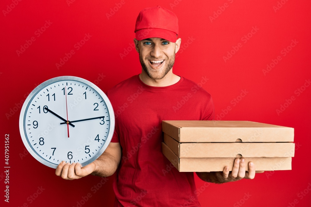 Young caucasian man holding delivery package and clock smiling and laughing hard out loud because funny crazy joke. Young caucasian man holding delivery package and clock smiling and laughing hard out loud because funny crazy joke.
