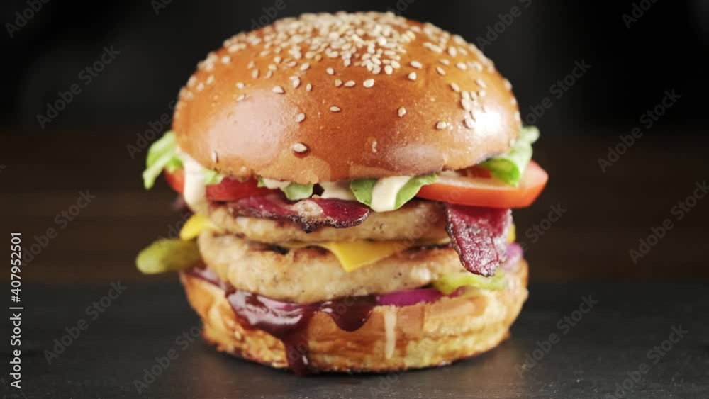 Hands in black gloves put juicy grilled chicken burger with double cutlet and cheese on the table on a black background. Hands in black gloves put juicy grilled chicken burger with double cutlet and cheese on the table on a black background.