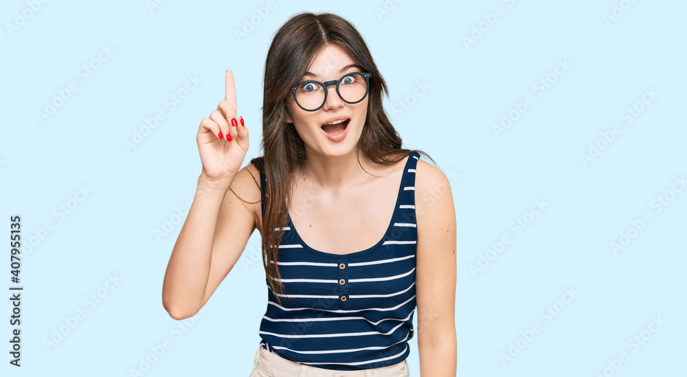 Young beautiful caucasian girl wearing casual clothes and glasses pointing finger up with successful idea. exited and happy. number one.