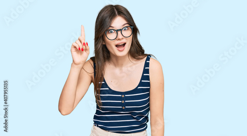 Young beautiful caucasian girl wearing casual clothes and glasses pointing finger up with successful idea. exited and happy. number one.