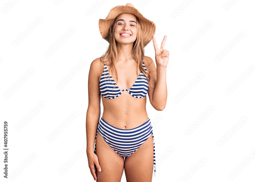 Young beautiful blonde woman wearing bikini and hat showing and pointing up with fingers number two while smiling confident and happy. Young beautiful blonde woman wearing bikini and hat showing and pointing up with fingers number two while smiling confident and happy.