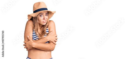 Young beautiful blonde woman wearing bikini and hat shaking and freezing for winter cold with sad and shock expression on face photo