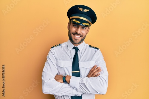 Canvastavla Handsome hispanic man wearing airplane pilot uniform happy face smiling with crossed arms looking at the camera
