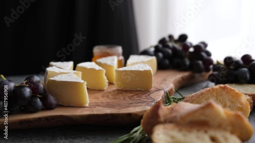 Brie or camembert cheese sliced on wooden cheeseboard served with grapes, figs and french bread