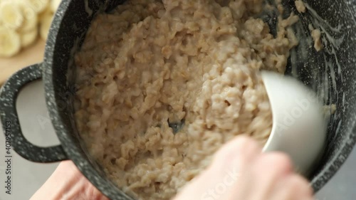 Stirring oatmeal porridge in cooking pan with a plastic spoon. Cooking healthy breakfast