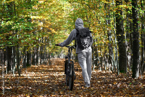 young man walks with a bicycle in the autumn forest on the road lined with yellow leaves