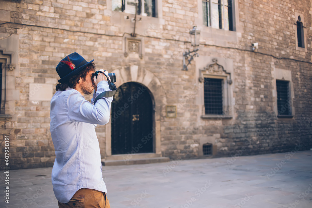 Trendy adult man taking shot with digital camera while standing at entrance of aged building