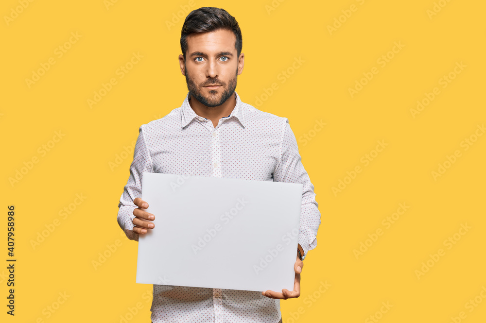 Handsome hispanic man holding blank empty banner thinking attitude and sober expression looking self confident Handsome hispanic man holding blank empty banner thinking attitude and sober expression looking self confident