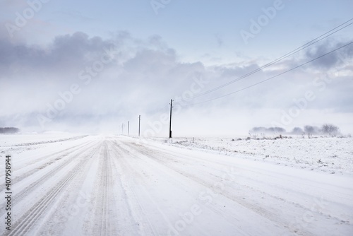 Snow-covered rural road through the field. Electricity line, transformer poles. Panoramic view from the car. Colorful clouds, dramatic sunset sky. Off-road, logistics, winter tires, remote village photo